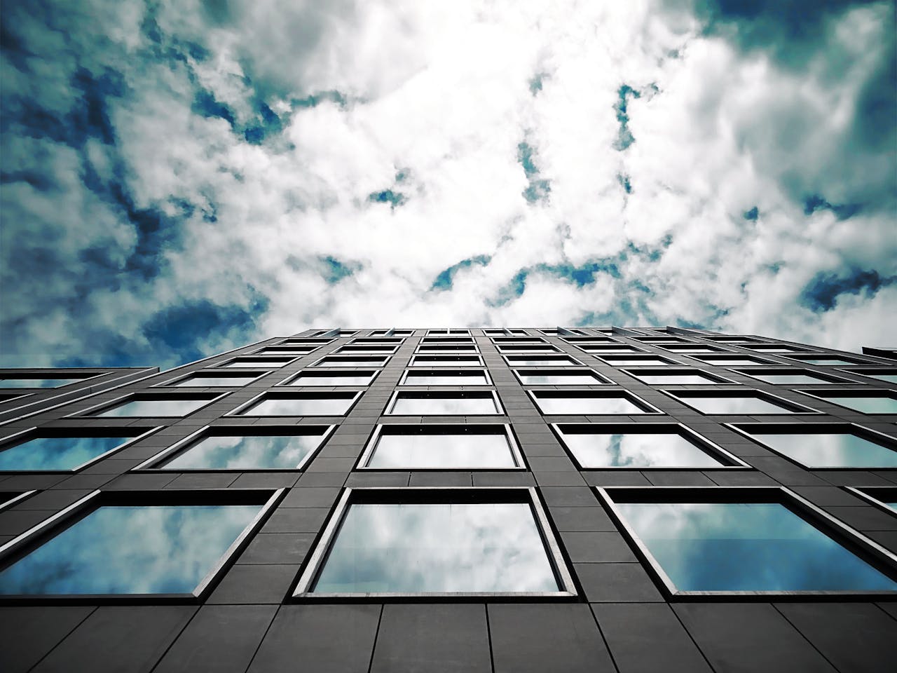 services-01 Low angle of a modern skyscraper reflecting clouds in its glass windows with a dramatic sky.